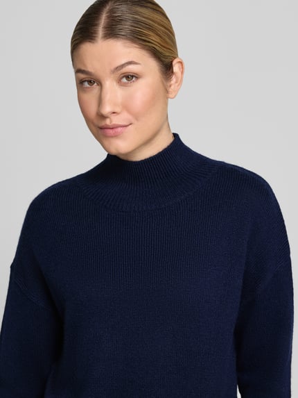 Frauenmodel trägt Strickpullover aus Kaschmir-Mix mit Woll-Anteil Modell 'Nina' von 0039 Italy in Dunkelblau, Nahaufnahme Oberkörper. Regular Fit, überschnittene Schultern, gerippte Abschlüsse, gerippter Stehkragen, Strick-Optik.