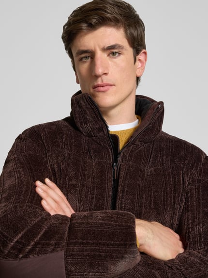 Männermodel trägt Pufferjacke mit abnehmbarer Kapuze von BOSS Orange aus Cord mit Struktur, Stehkragen, Reißverschluss, Nahaufnahme Oberkörper.