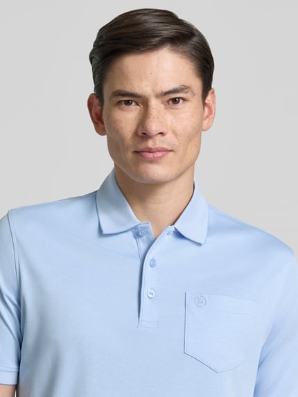 Męski model nosi Regular Fit Poloshirt mit Brusttasche und Label-Stitching von bugatti, jasnoniebieski, kołnierzyk polo, listwa guzikowa, wyhaftowane logo, brustasza, długość tyłu w rozmiarze M 70 cm, z przodu, zbliżenie górnej części ciała.