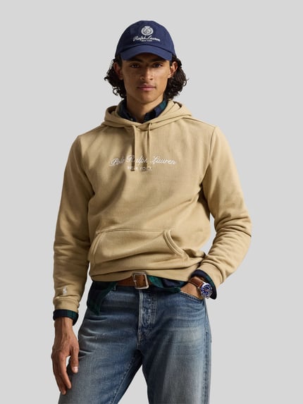 Männermodel trägt Relaxed Fit Hoodie aus Baumwoll-Mix von Polo Ralph Lauren in Beige mit Logo, kombiniert mit Jeans, Ganzkörperansicht von vorne.
