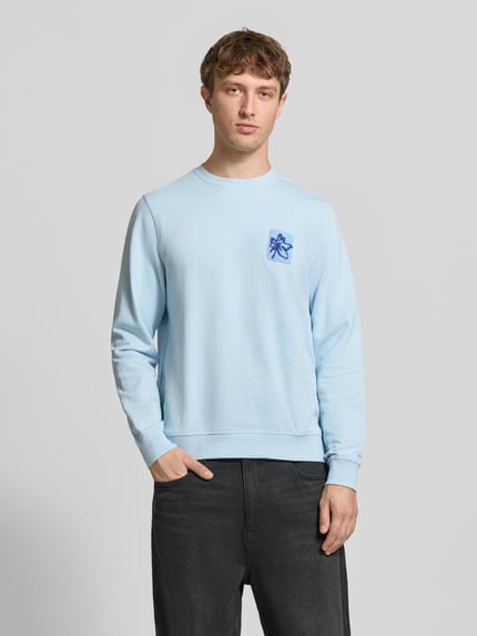 Männermodel trägt Regular Fit Sweatshirt mit floraler Applikation Modell 'Felica' von Blend, reine Baumwolle, hellblau, Ganzkörperansicht von vorne.