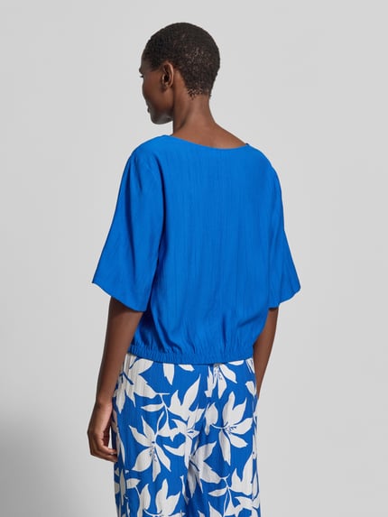 Vrouwenmodel draagt Relaxed Fit Blusentop uit viscosemix van s.Oliver RED LABEL, all-over bloemenmotief, satijnlook, plooien, korte mouw, rugaanzicht, ganzebody.
