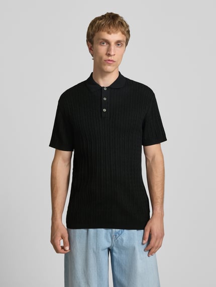 Mannenmodel draagt Slim Fit Strick-Poloshirt met kabelpatroon model 'EMIL' van Jack & Jones, katoenmix met viscose, slim fit, polokraag en knoopsluiting, kleur zwart, vooraanzicht halve lichaamsopname.