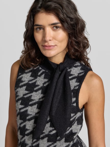 Frauenmodel trägt Pullunder mit Schluppe Modell 'VMMARLENA' von VERO MODA in Schwarz-Grau, Hahnentritt im Jacquardstrick, Nahaufnahme Oberkörper.