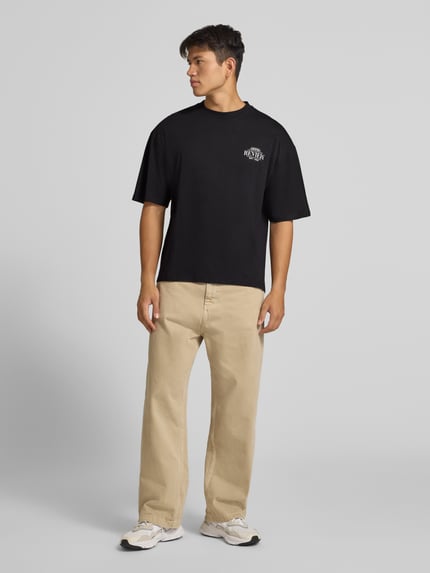Männermodel trägt Regular Fit T-Shirt aus reiner Baumwolle mit rückseitigem Print von REVIEW, czarny, jasnobeżowe spodnie, Szerokość w rozmiarze M: 67 cm, Ganzkörperansicht von vorne