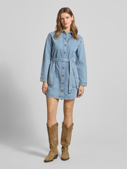 Frauenmodel trägt Minikleid in Denim-Optik mit Umlegekragen von Calvin Klein Jeans, reine Baumwolle, tailliert, langärmelig, Knopfleiste, Taillenband, Taschen, heller Blauton, strukturierte Oberfläche, Ganzkörperansicht von vorne.