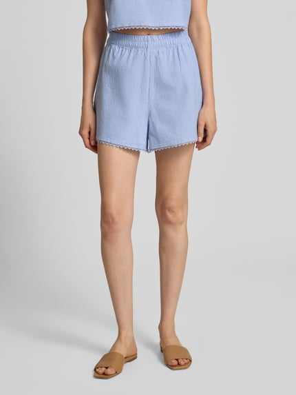 Kobieta nosi Regular Fit Shorts mit Spitzenbesatz Modell 'Feoly' od American Vintage, bawełna, szerokość w rozmiarze S 31 cm, jasnoniebieski, krótkie spodenki, widok z przodu, zbliżenie na dolną część ciała.