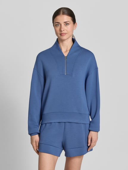 Modelka nosi Sweatshirt aus Viskose-Mix mit Reißverschluss Modell 'davidson' od VARLEY w kolorze niebieskim, krój regular fit, V-dekolt, widoczny zamek, miękka faktura, damska bluza z dodatkiem stretchu, widok na cały przód, zdjęcie przedstawia górną część ciała