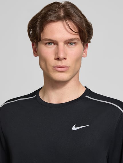 Männermodel trägt T-Shirt mit Rundhalsausschnitt und Logo von NIKE TRAINING in Schwarz mit Kontraststreifen, Nahaufnahme Oberkörper. Regular-Fit, Rückenlänge bei Größe M: 74 cm.