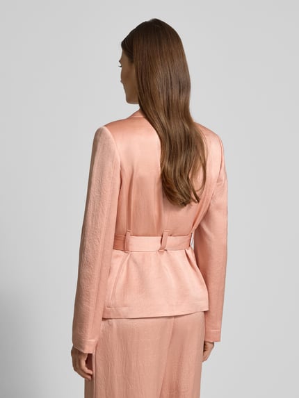 Frauenmodel trägt Blazer mit Reverskragen von Marc Cain aus Acetat-Mix in zartem Rosé, Taillengürtel, taillierter Schnitt, Rückenlänge 61 cm, Brustweite 46 cm, Ärmellänge 62 cm, Ganzkörperansicht Rückansicht.