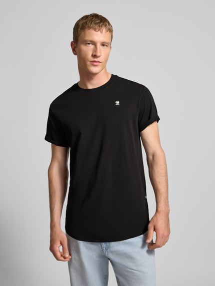 Männermodel trägt T-Shirt mit Label-Detail von G-Star aus reiner Bio-Baumwolle, gerader Schnitt, Rundhalsausschnitt, schwarze Farbe, fixierte Ärmelumschläge, Rückenlänge 76 cm bei Größe L, Ganzkörperansicht von vorne.