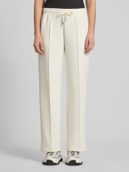 Frauenmodel trägt Sweatpants mit Label-Applikation Modell 'Talila' von JOOP! in creme, gerader Schnitt, elastischer Bund, Ganzkörperansicht von vorne.