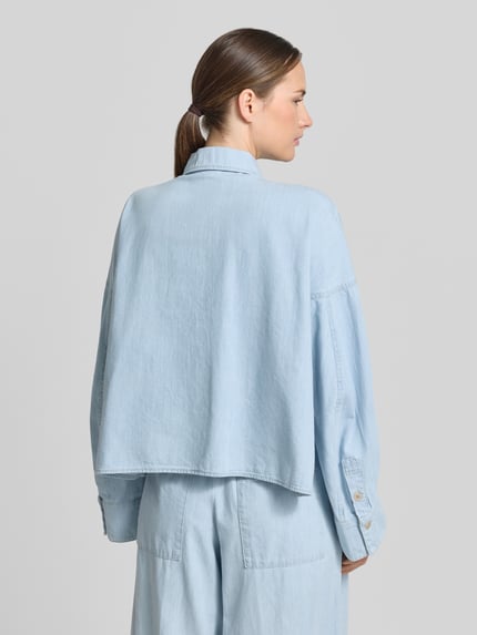 Frauenmodel trägt Relaxed-Fit Hemdbluse in Denim-Optik Modell 'Oshia' von Drykorn aus Reine Baumwolle, langärmelig, Rückenlänge 55 cm bei Größe 36, Ganzkörperansicht Rückansicht.