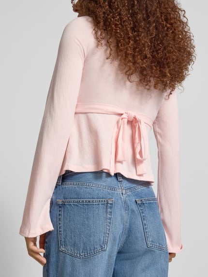 Männermodel trägt Regular Fit Langarmshirt in Wickel-Optik Modell 'PELLY' von Only, różowa struktura, wiązanie, dżinsy, krój regular fit, głęboki dekolt, dzwonowate rękawy, tekstura miękka, całkowity widok z tyłu.