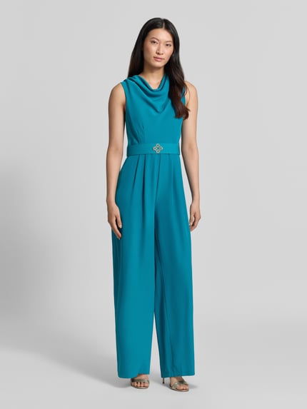 Frauenmodel trägt Jumpsuit mit Neckholder von Rinascimento in Türkis, Material-Mix mit Stretch, Stoffgürtel, taillierte Passform, Ganzkörperansicht von vorne.