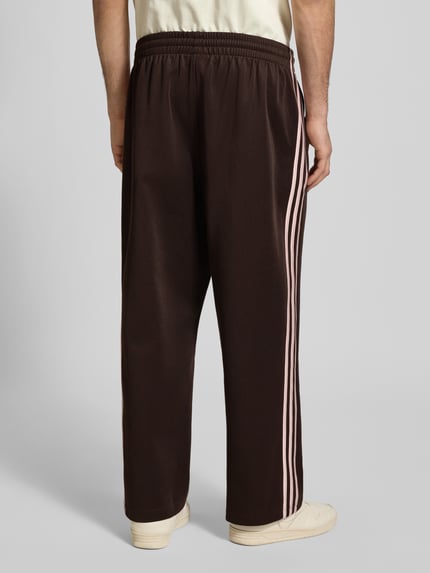 Mężczyznamodel nosi Straight Fit Sweatpants mit Logo-Stitching Modell 'Firebird' od adidas Originals, bawełniana mieszanka, krój straight fit, elastyczny pas, ozdobne przeszycie, widoczne logo, spodnie dresowe, widok całej sylwetki z tyłu.