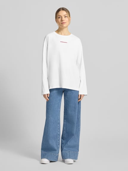 Vrouwenmodel draagt Oversized langarmshirt van pure katoen FIETAA SMILE van ARMEDANGELS, uni wit, fijnrib, logo-smile-stiksel, vooraanzicht hele lichaam