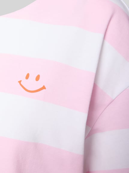 Vrouwenmodel draagt Pyjama-Oberteil met Motiv-Print van Mey, roze-witte strepen, oranje smiley, zachte stof, detailopname schouder.