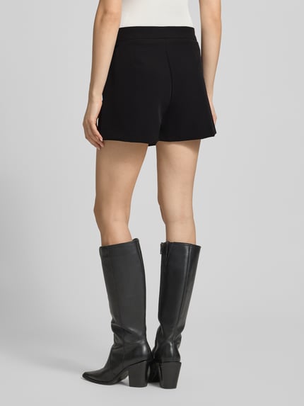 Frauenmodel trägt Regular Fit Minirock mit integrierter Shorts Modell 'Sofia' von JJXX in Schwarz, glatte Textur, Ganzkörperansicht Rückansicht, Damen Minirock, elastischer Material-Mix, Wickel-Optik.