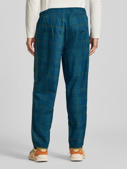 Männermodel trägt Relaxed Fit Trackpants aus reiner Baumwolle von PUMA mit Tartan Allover-Muster in Blau, Ganzkörperansicht Rückansicht.