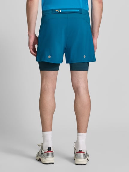 Männermodel trägt Regular Fit Shorts mit integrierten Tights Modell 'Road' von ASICS TIGER in Blau, elastischer Bund, Logo-Detail, Ganzkörperansicht Rückansicht. Bundweite Größe M: 38 cm, Innenbeinlänge: 12 cm.