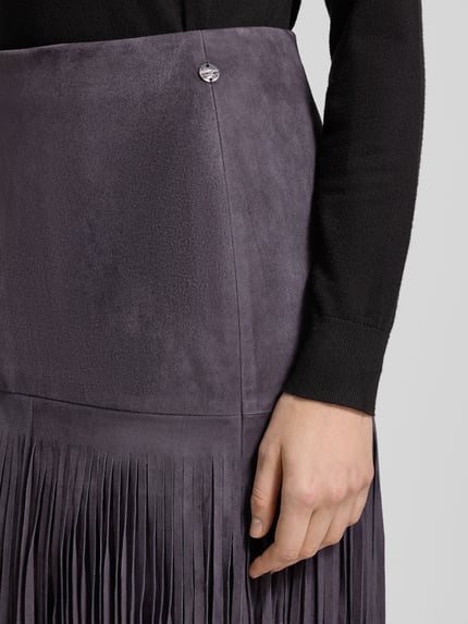 Kobiece modelka nosi Lederrock mit Fransen und rückseitigem Reißverschluss od Marc Cain, spódnica midi, naturalna skóra, prosty krój, frędzle, zamek błyskawiczny z tyłu, zbliżenie na górną część spódnicy