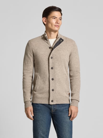 Männermodel trägt Cardigan mit Stehkragen Essential PATCH von BARBOUR in beige, Strickoptik, durchgehende Knopfleiste, langarm, unifarben, gerippte Abschlüsse, Ganzkörperansicht von vorne.