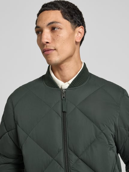 Männermodel trägt Regular Fit Steppjacke mit Stehkragen van Superdry in donkergroen met Stiksels, ritssluiting, Steekzakken, elastische mouwboorden, Nahaufnahme Oberkörper, Heren