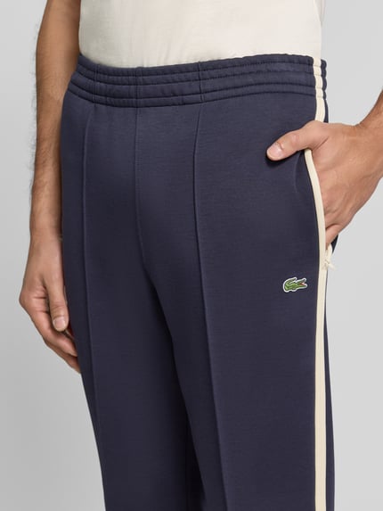 Männermodel trägt Regular Fit Jogpants aus Baumwoll-Mix von Lacoste in Dunkelblau mit cremefarbenen Streifen, Nahaufnahme Oberkörper, Herren Weite Hose von Lacoste.