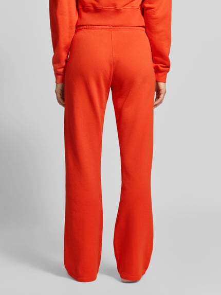 Frauenmodel trägt Sweatpants aus Baumwoll-Modal-Mix von Juvia in leuchtendem Orange, lockere Passform, elastischer Bund, Ganzkörperansicht Rückansicht.