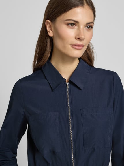 Kobiece model prezentuje sukienkę koszulową Hemdblusenkleid mit Reißverschluss Modell 'NETTI' od Soyaconcept z mieszanki bawełny, linia a, sukienka midi, zamek błyskawiczny, elastyczna tasiemka w talii, długość tyłu w rozmiarze s: 121 cm, szerokość w rozmiarze s: 42 cm, długość rękawów w rozmiarze s: 60 cm, granatowa, prosta faktura, zbliżenie na górną część tułowia.