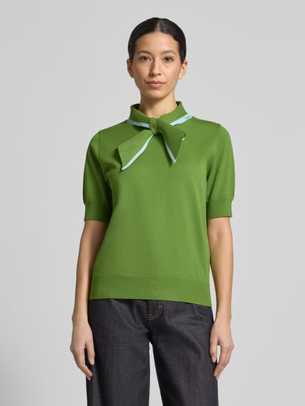 Frauenmodel trägt Regular Fit Poloshirt aus Viskose-Mix Modell 'JONDA' von Essentiel Antwerp, Optik: Unifarben, Kontraststreifen, Polokragen mit Schleife, Ärmelform: Kurzarm, Ärmelabschluss: Gerippt, Rumpfabschluss: Gerippt, Materialverarbeitung: Taschen, Farbe grün, glatte Textur, Ganzkörperansicht von vorne.
