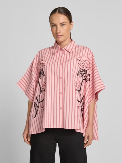 Vrouwenmodel draagt roze-wit gestreepte oversized blouse met korte mouwen van puur katoen model 'JONKOE' van Essentiel Antwerp, vooraanzicht bovenlichaam.