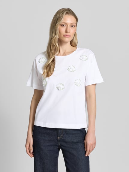 Modelka kobieca ma na sobie T-Shirt mit Stitchings und Rundhalsausschnitt von More & More, biała bawełna, krój regular fit, długość tyłu w rozmiarze 36: 50 cm, widok całej sylwetki z przodu.