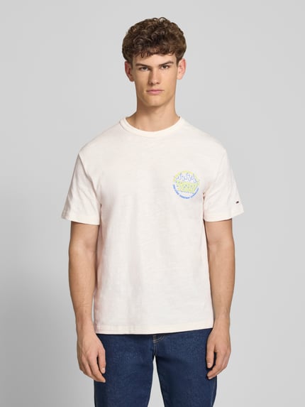 Męski model nosi Relaxed Fit T-Shirt aus reiner Baumwolle von Tommy Jeans, jasny kolor, nadruk z logo, jersey, krótki rękaw, widok z przodu, ujęcie całej sylwetki.