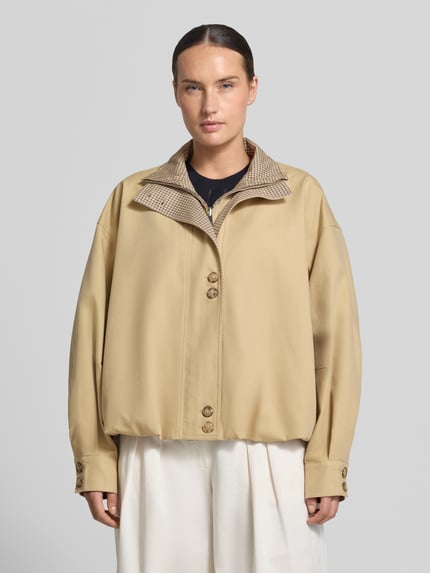 Kobieta modelka nosi Relaxed Fit Jacke mit Lyocell-Anteil od Rich & Royal, mieszanka bawełny i lyocellu, stójka, plisa, beżowy kolor, długość tyłu w rozmiarze 36: 58 cm, szerokość ramion w rozmiarze 36: 60 cm, szerokość klatki piersiowej w rozmiarze 36: 67 cm, długość rękawów w rozmiarze 36: 54 cm, całkowity widok z przodu.