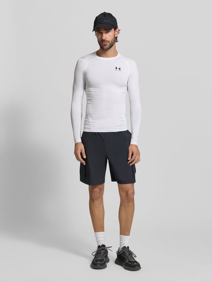 Männermodel trägt Slim Fit Longsleeve mit Logo-Print von Under Armour in Weiß, elastischer Material-Mix, Rundhalsausschnitt, Ganzkörperansicht von vorne.