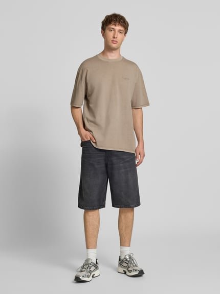 Männermodel trägt Oversized T-Shirt mit Label-Stitching von Pegador in Beige, reine Baumwolle, Rundhalsausschnitt, Ganzkörperansicht von vorne.