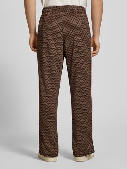 Männermodel trägt Loose Fit Sweatpants mit Logo-Muster Modell 'FIREBIRD' von adidas Originals, Optik:Allover-Muster, Materialverarbeitung: Sweat, Ganzkörperansicht Rückansicht.