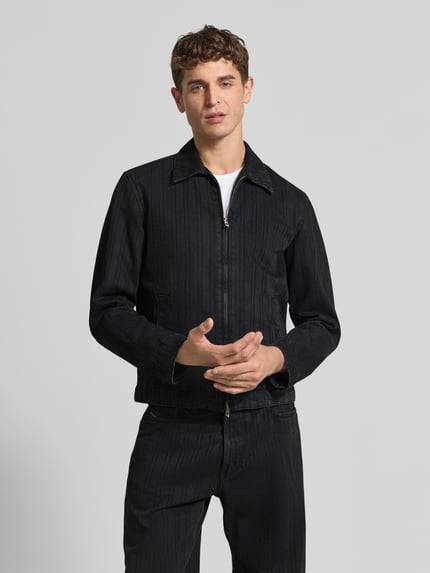 Mężczyzna nosi Slim Fit Jeansjacke aus Baumwoll-Mix von Diesel w kolorze czarnym, struktura prążkowana, przód z dwukierunkowym zamkiem, kołnierz koszulowy, kieszenie boczne, krój slim fit, długość tyłu w rozmiarze M: 64 cm, szerokość ramion w rozmiarze M: 46 cm, długość rękawa w rozmiarze M: 65 cm, zdjęcie całej sylwetki z przodu.