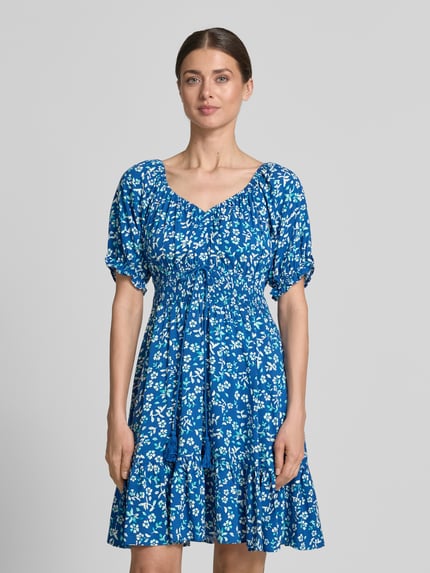 Vrouwenmodel draagt Minikleid aus Viskose mit Kordelzug und Quasten van Apricot in helder blauw met wit bloemenpatroon, getailleerd model, ronde hals met ruches, mouwen met ruches, tunnelkoord met kwastdetails, smokdetails, zuiver viscose, ruglengte maat S: 82 cm, borstwijdte: 34 cm, mouwlengte: 21 cm, Ganzkörperansicht van voren.