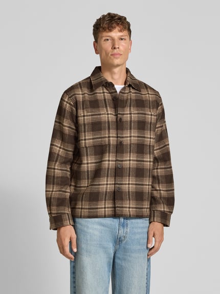 Männermodel trägt Freizeithemd mit durchgehender Knopfleiste von Selected Homme, kariertes Muster in Braun, Allover-Optik, Langarm, Ganzkörperansicht von vorne.