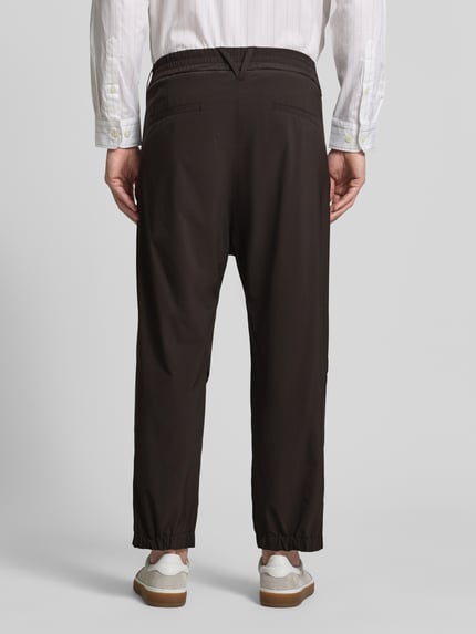 Männermodel trägt Relaxed Fit HOSE mit Bundfalten Modell 'Lirog' von Drykorn, Dunkelbraun, Elastischer-Material-Mix, Ganzkörperansicht Rückansicht, Herren, Bundweite 41 cm, Innenbeinlänge 62 cm, Eingriffstaschen, Gesäßtasche, Knopf- und Reißverschluss.