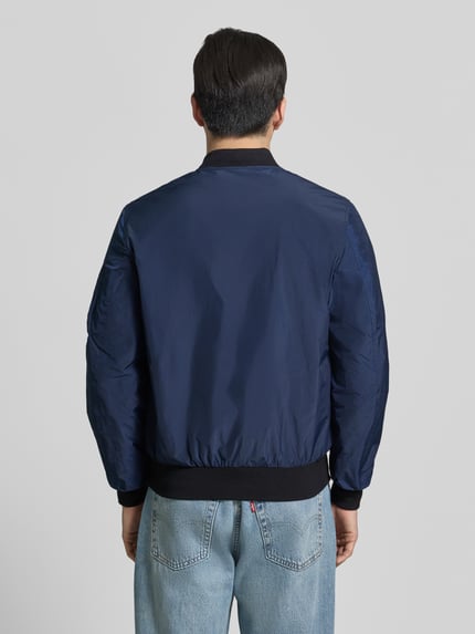 Männermodel trägt Bomberjacke mit Label-Patch und Eingrifftaschen von Original Bombers in Dunkelblau, Gerader-Schnitt, Ganzkörperansicht Rückansicht. Rückenlänge 67 cm, Schulterbreite 43 cm, Brustweite 53 cm, Ärmellänge 68 cm, Reißverschluss, Reißverschlusstasche am Ärmel, Druckknopfverschluss, Gerippte-Abschlüsse.