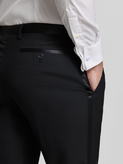 Mężczyznamodel nosi Slim Fit Anzughose mit Gesäßtaschen von MCNEAL, kolor czarny, materiał z domieszką wiskozy, z tylną kieszenią na guzik, widoczne kanty, krój slim fit, Szerokość w rozmiarze 50: 45 cm, długość nogawki od wewnątrz 83 cm, widok detailaufnahme tylna część.