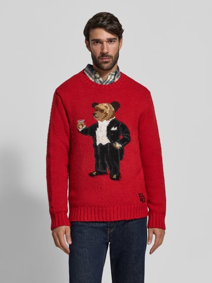 Männermodel trägt Regular Fit Pullover aus reiner Wolle mit Polo-Bear-Intarsie von Polo Ralph Lauren in Rot, Ganzkörperansicht von vorne. Herren Pullover.