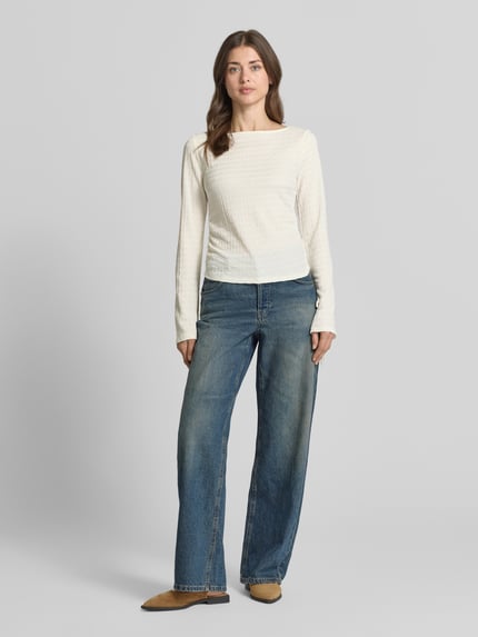 Vrouwenmodel draagt shirt met lange mouwen Regular Fit Langarmshirt met Binde-Detail model 'HAZEL' van Vero Moda, look: effen, structuurpatroon, pasvorm: regular fit, plooien, boothals, trompetmouwen met strikdetail, Ganzkörperansicht von voren.