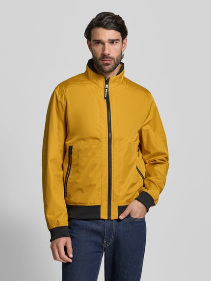 Männermodel trägt Regular Fit Jacke mit Stehkragen von MCNEAL in Gelb, Reißverschluss, Eingrifftaschen, elastische Abschlüsse, Ganzkörperansicht von vorne. Rückenlänge 64 cm, Schulterbreite 43 cm, Brustweite 55 cm, Ärmellänge 67 cm.