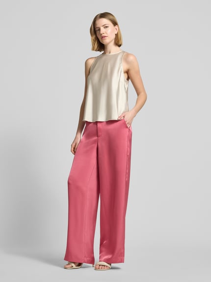 Frauenmodel trägt Satinhose mit angedeuteten Gesäßleistentaschen Modell 'Emmett' von Neo Noir, Satin, Wide-Fit, rosa, Eingrifftaschen, Haken- und Reißverschluss, Bundweite 39 cm, Innenbeinlänge 86 cm, Ganzkörperansicht von vorne.