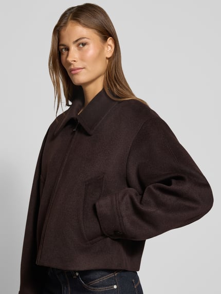 Frauenmodel trägt Jacke mit Eingrifftaschen Modell 'CANDYX' von MANGO in Dunkelbraun, Material-Mix mit Umlegekragen, Nahaufnahme Oberkörper.
